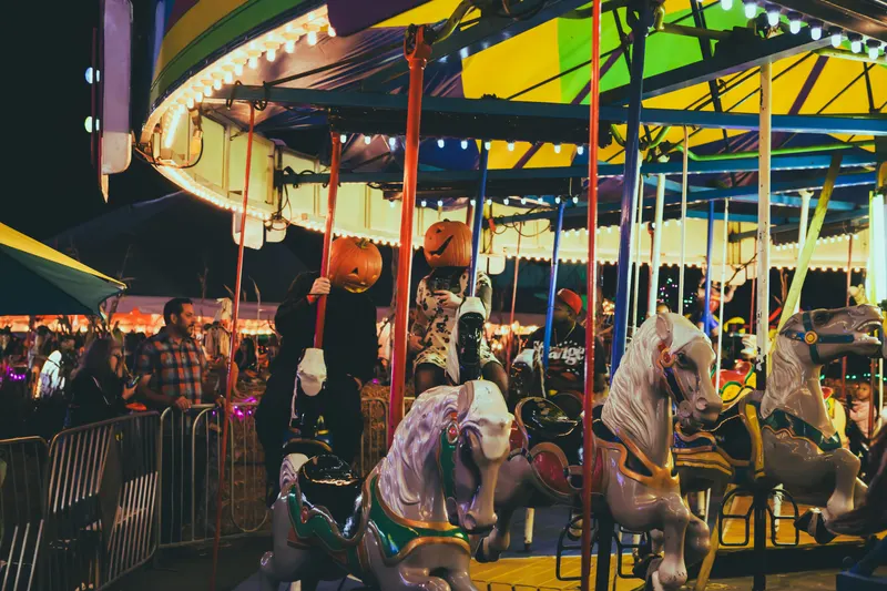 Riders wearing carved-pumpkin heads on the carousel horses at night