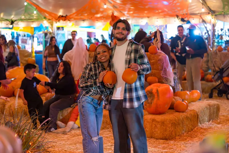 A couple posing with pumpkins on hay bales under the lit tent