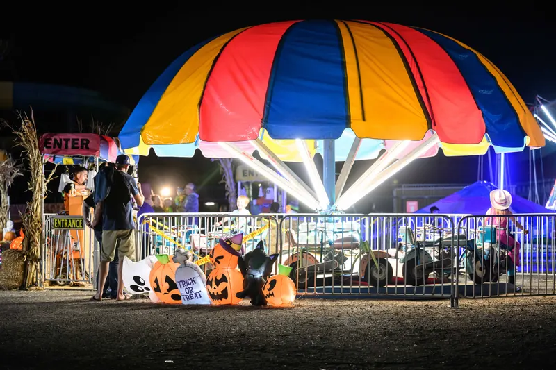 A kiddie ride under a striped canopy at night with inflatable jack-o'-lanterns and a trick-or-treat sign at the entrance