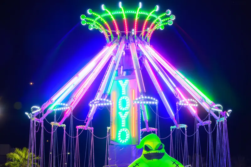 The YoYo swing ride lit in neon purple and green at night with a giant inflatable Oogie Boogie at its base