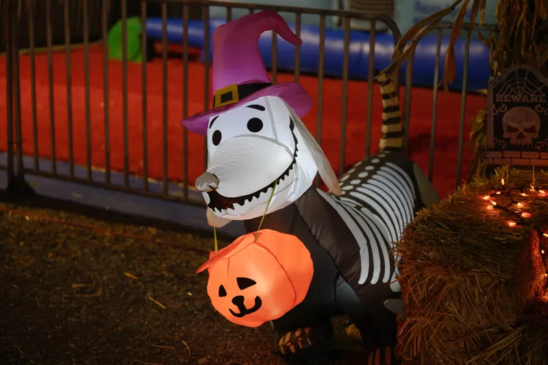 An inflatable ghost dog in a witch hat holding a jack-o'-lantern bucket beside a hay bale