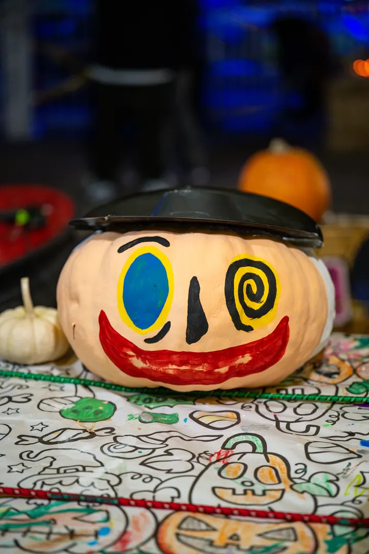 A pumpkin painted with a smiling face by a child, sitting on a coloring sheet at the craft table