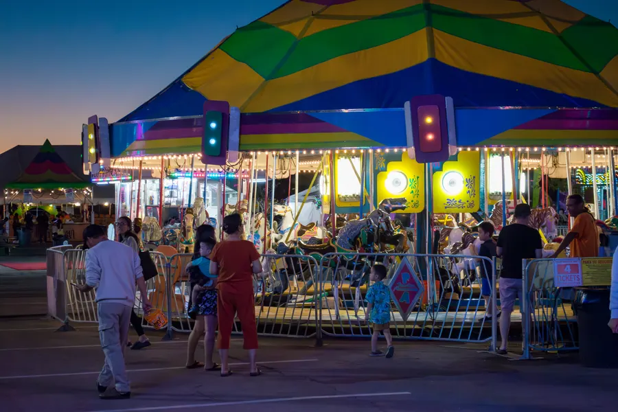 Families lining up at the carousel under its striped canopy at dusk