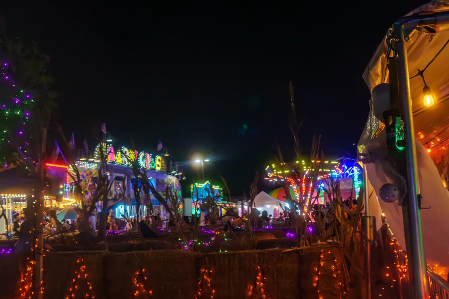 The pumpkin tent glowing at night with the rides lit behind it