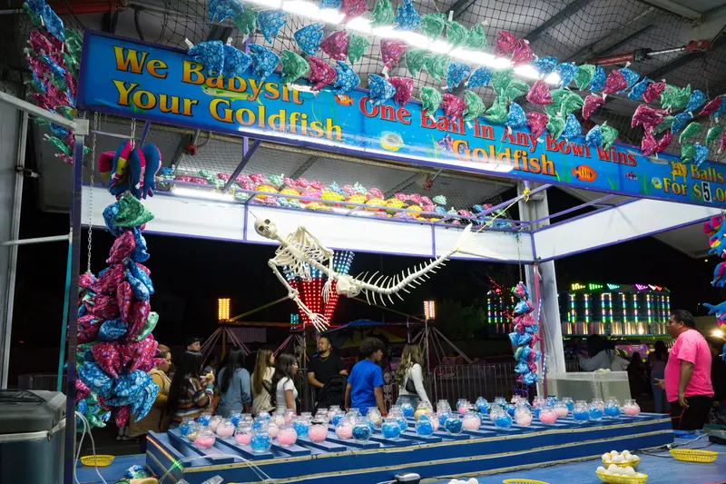 Guests at the goldfish bowl toss booth lit up at night