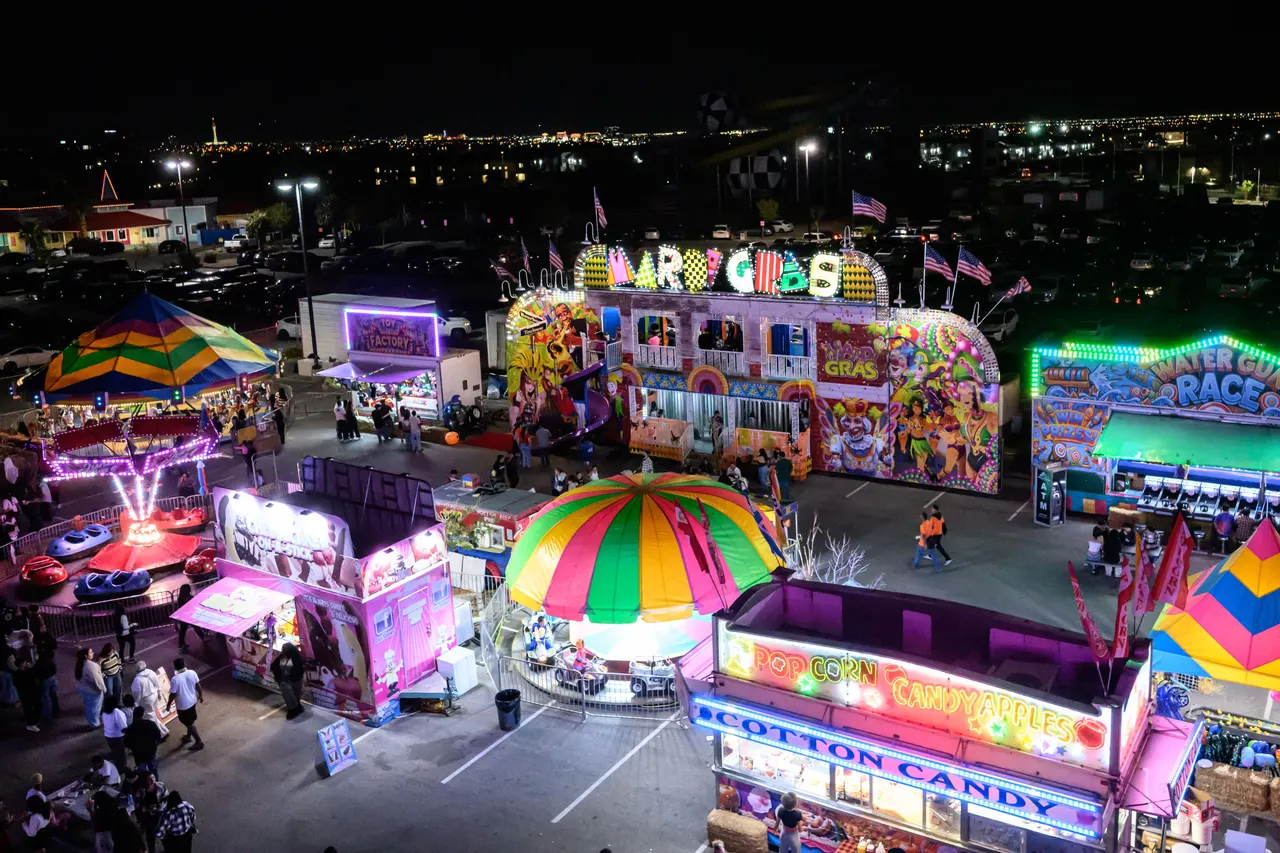 Vegas Pumpkin Patch lit up at night in the Cowabunga Bay parking lot, with game booths, rides and food stands surrounded by parking and the Las Vegas skyline on the horizon