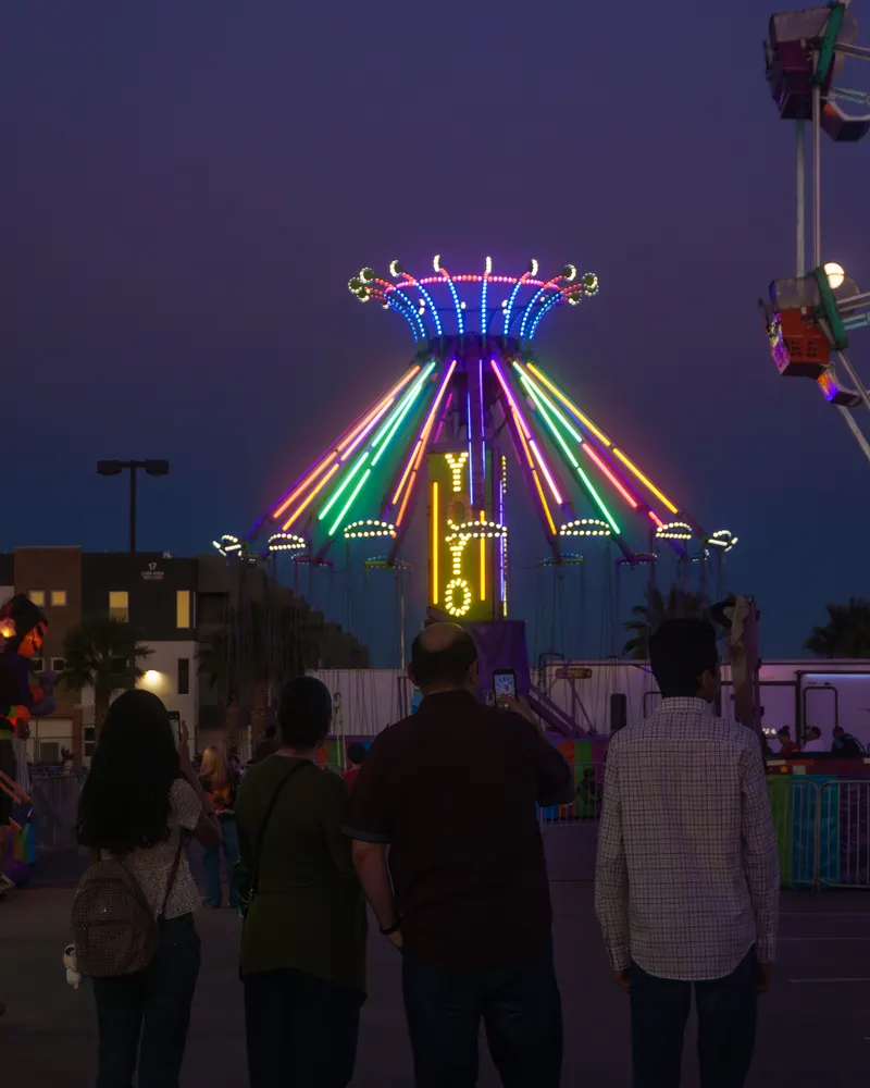 Four people standing together at dusk watching the swing ride lit in green, blue and pink